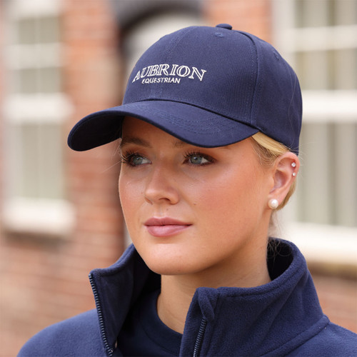 Woman wearing a navy Aubrion Equestrian baseball cap with embroidered logo, outdoor lifestyle shot.
