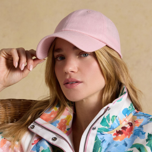 Model wearing a pale pink Joules baseball cap with curved peak, shown close up against a neutral studio background.