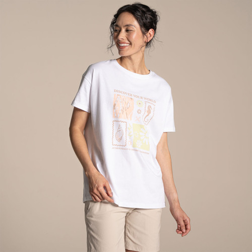 Model wearing a women’s white “Discover Your World” graphic T-shirt with pastel print, styled with beige shorts, studio background.