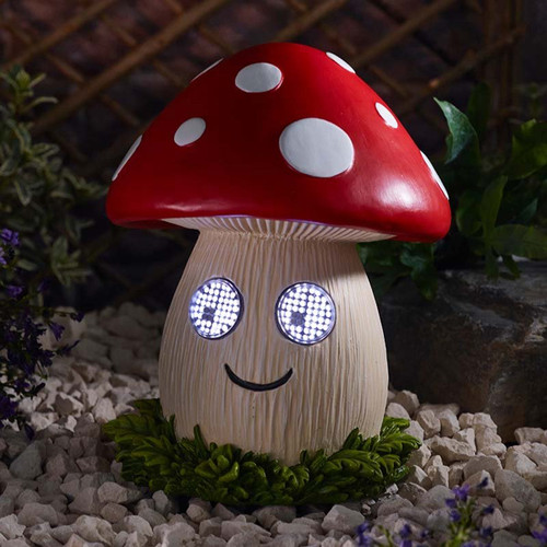 Smiling mushroom-shaped garden light with a red and white spotted cap and illuminated LED eyes, glowing at night among decorative stones.