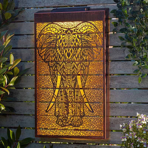 Illuminated decorative garden wall panel featuring an intricate elephant design, glowing warm amber against a wooden fence backdrop.