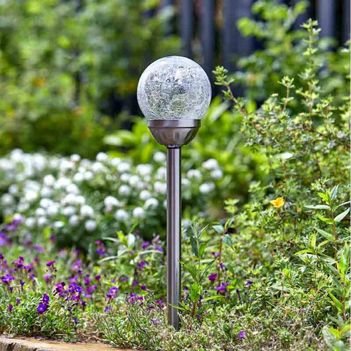 Stainless steel solar garden stake light with a crackle-glass globe, positioned among flowers and greenery during daylight.