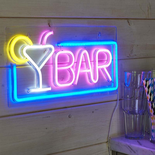 Neon cocktail bar sign with a martini glass icon and the word “BAR” in pink, outlined in blue, mounted on a wooden wall beside drinking glasses and straws.