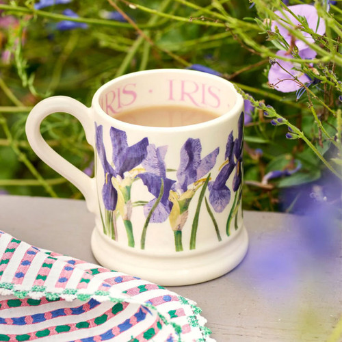 Emma Bridgewater blue iris half-pint mug filled with tea, styled outdoors among garden flowers.