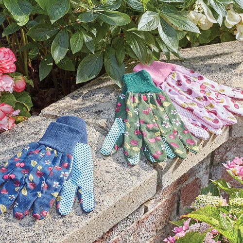 Three pairs of cherry-pattern gardening gloves in blue, green, and pink laid out on a stone garden wall