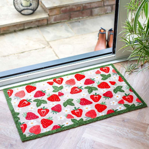 Rectangular doormat with a strawberry pattern and green border, placed by a glass door.