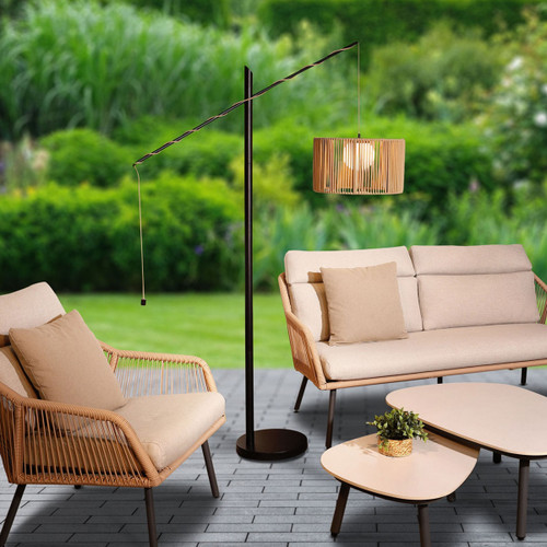 Outdoor floor lamp with a latte woven shade and black metal stand, styled beside a garden lounge set on a patio.