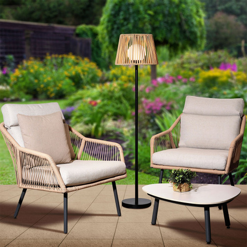 Latte outdoor floor lamp with a slatted shade on a black stand, styled with patio armchairs and a coffee table in a garden setting.