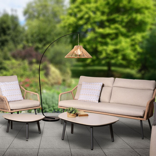 Ballagio latte arched floor lamp with woven shade over an outdoor seating set on a patio, with a garden backdrop.
