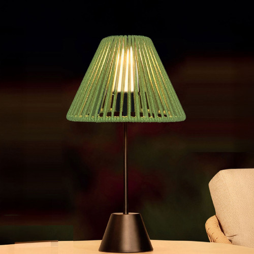 Sage green woven table lamp with a black base, glowing warmly on an outdoor side table.