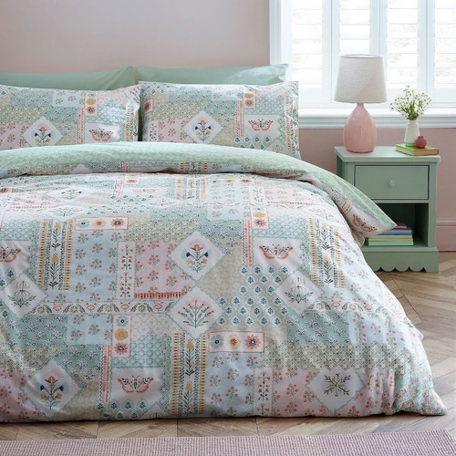 Patchwork floral duvet cover set in soft sage green and pastel tones, styled on a double bed with matching pillowcases in a bright, airy bedroom.