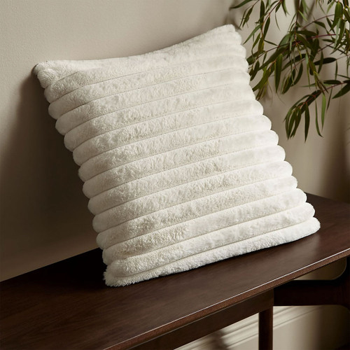 Cream ribbed faux fur cushion styled on a wooden bench, creating a cosy and neutral home interior look.