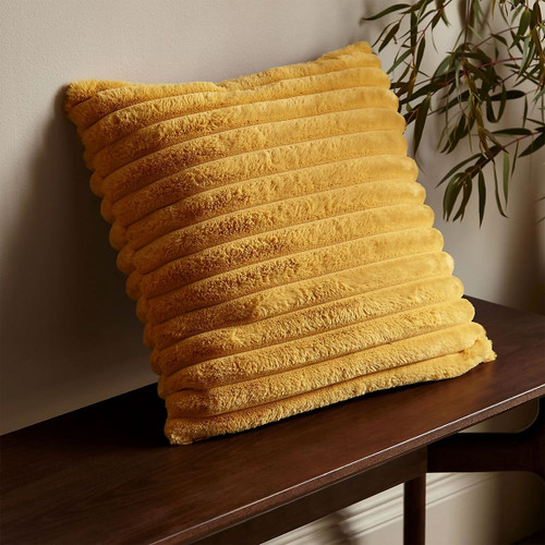 Mustard yellow ribbed faux fur cushion styled on a wooden bench with greenery in the background