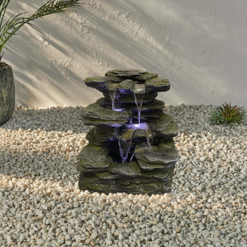 Rock-effect waterfall fountain lit with blue LEDs, shown outdoors on decorative gravel.