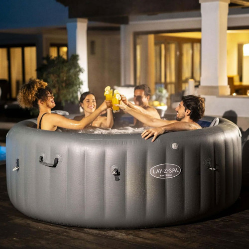 Friends relaxing in a grey inflatable hot tub at night, raising drinks together in a garden setting.