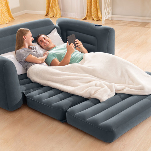 Grey inflatable pull-out sofa bed with built-in armrests and cup holder in a living room.