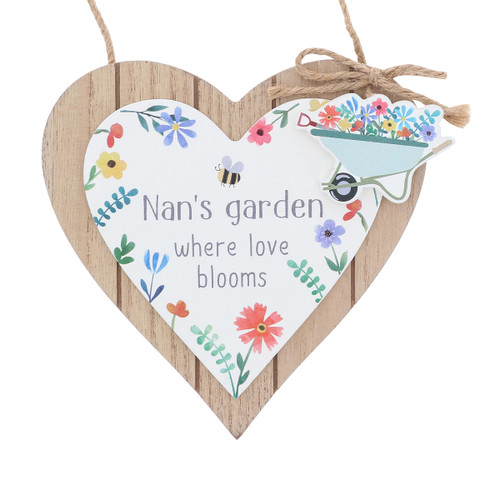 Wooden heart-shaped hanging plaque with a white heart panel reading “Nan’s garden where love blooms,” decorated with colourful flowers, a bee, and a wheelbarrow full of flowers, finished with a twine hanger and bow.