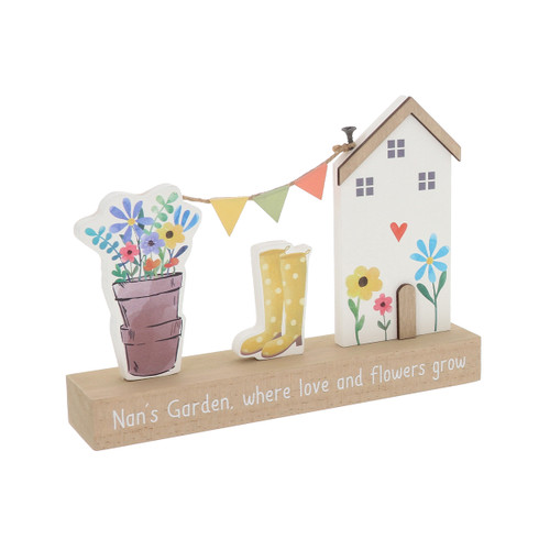 Freestanding wooden table plaque featuring a decorative house with flowers and heart detail, colourful bunting, yellow spotted wellington boots and a flower pot, set on a wooden base printed with the words “Nan’s Garden, where love and flowers grow”.