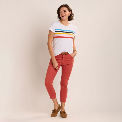 Woman wearing coral cropped slim-fit trousers styled with a white T-shirt featuring multicoloured chest stripes and brown suede loafers.