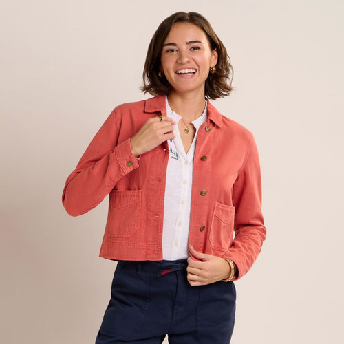 Model wearing a coral cropped jacket with brass buttons and patch pockets, styled over a white blouse and navy trousers.