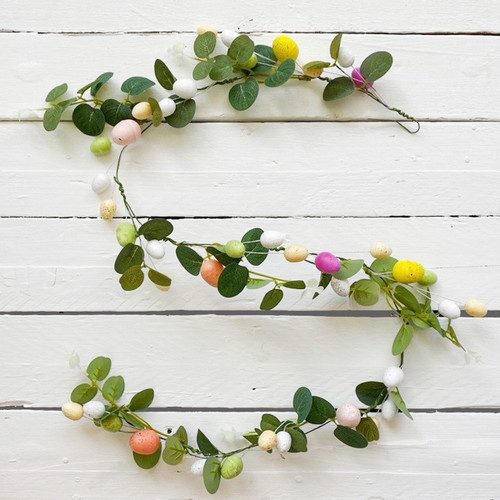 Easter garland made from green faux foliage and pastel speckled eggs, arranged against a white wooden background.