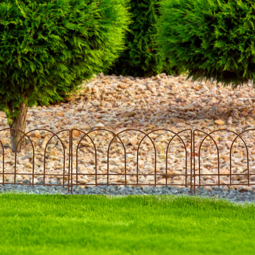 Rust-finish metal border edging with a classic arched design, separating a gravel bed and green lawn in front of evergreen shrubs.
