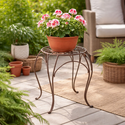 Terracotta plant pot with pink flowers displayed on a brown metal plant stand on a patio, with outdoor seating and greenery in the background.