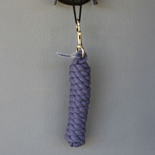 A purple, intricately braided keychain hangs from a black cord against a plain gray wall, evoking a sense of simplicity and elegance.
