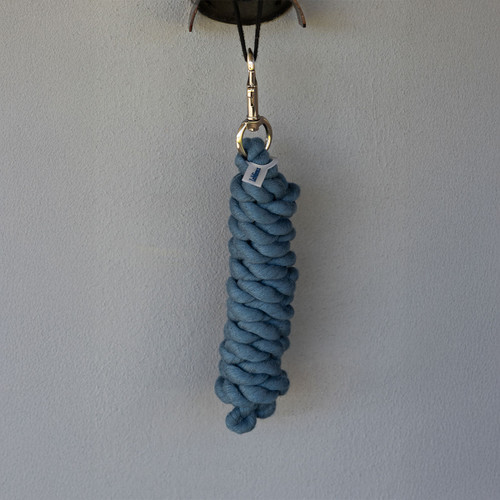 Handmade blue cotton rope keychain with a braided design hangs from a brass hook against a light grey wall, conveying simplicity and craftsmanship.