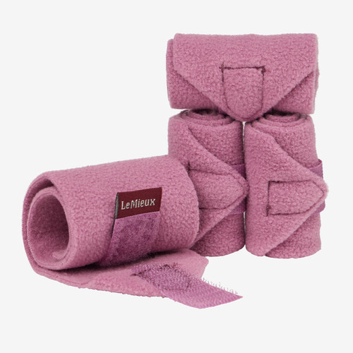 Four pink fleece equestrian bandages are neatly rolled, with one partially unrolled, revealing a velcro strap and "LeMieux" label. Clean, organized look.
