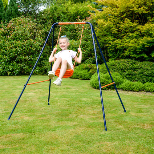 Girl playing on a Hedstrom garden swing set with orange seat and metal frame on a lawn.