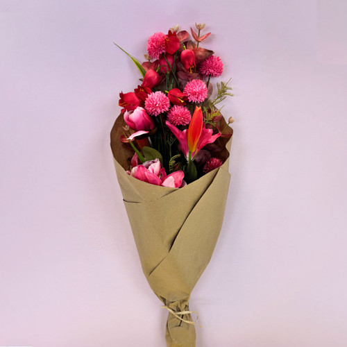 A neatly wrapped bouquet of pink and red flowers in brown paper, standing upright against a pale background.