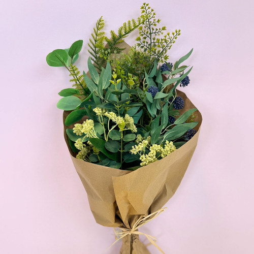 A neatly wrapped bouquet of green foliage with light yellow flowers and textured leaves standing upright against a light background.