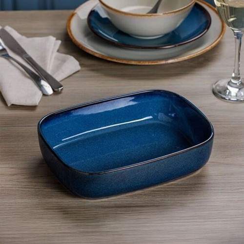 Blue rectangular ceramic baking dish on dining table with plates, cutlery, and wine glass, modern glazed oven dish table setting