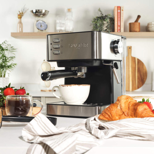 Salter manual espresso machine on a kitchen counter with a cup, pastries and fruit arranged around it.