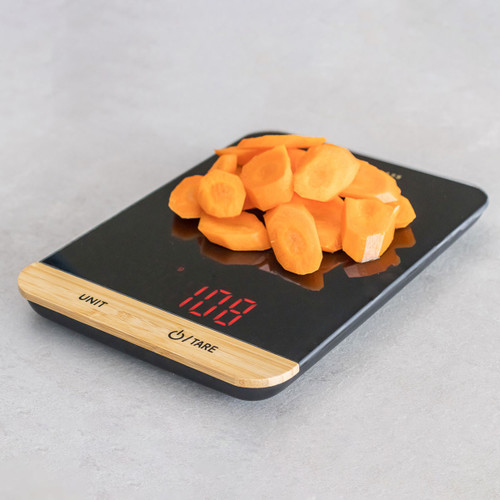 Sliced carrots on a black digital kitchen scale displaying weight in red LED numbers.