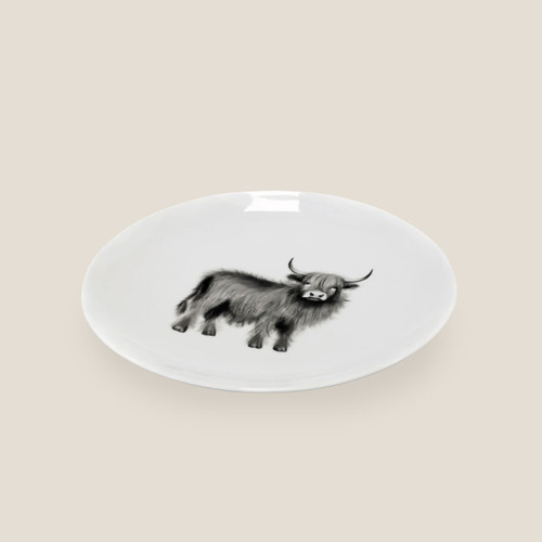 White ceramic plate featuring a Highland cow illustration in the centre on a plain background.