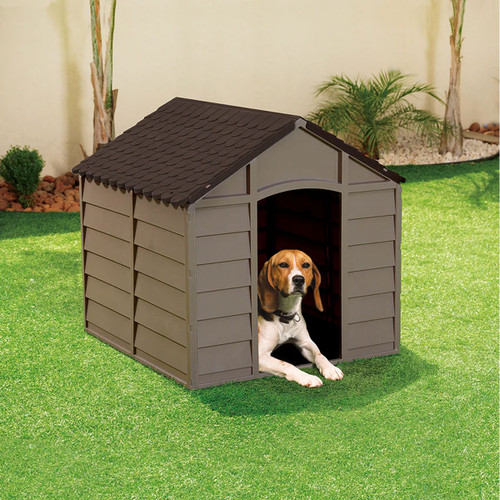 Brown plastic dog kennel with pitched roof, featuring a small dog lying in the doorway on a green lawn