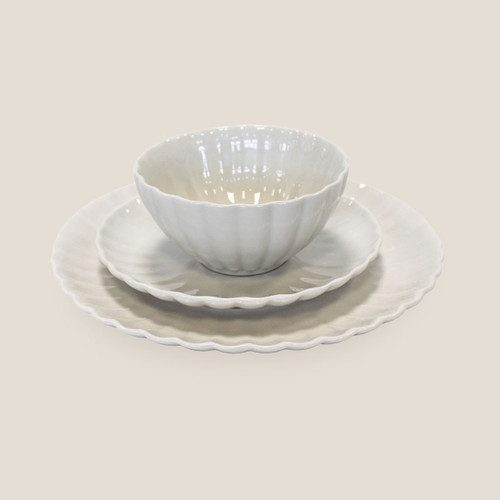 White stoneware bowl placed on matching scalloped side plate and dinner plate, shown at an angled front view on a light background.