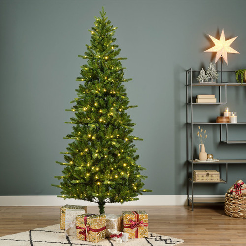 Slim pre-lit artificial Christmas tree with warm white LED lights, styled in a contemporary living room with wrapped Christmas presents and festive seasonal décor.