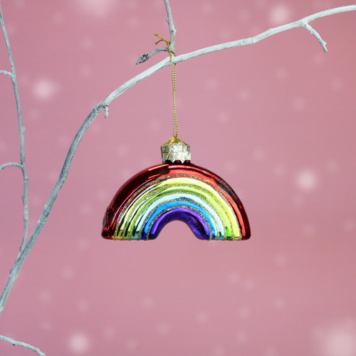 Rainbow-shaped Christmas decoration with colourful glitter-edged stripes and a gold hanging cord, displayed against a soft pink background.