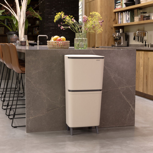 Brabantia SortUp dual recycling bin in Soft Beige standing beside a kitchen island in a modern kitchen interior.