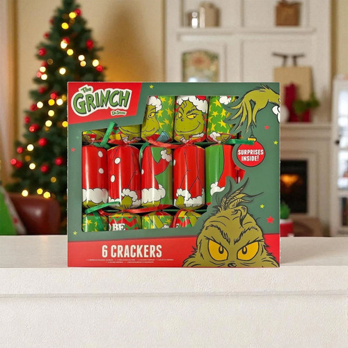 The Grinch Christmas cracker set featuring six festive crackers in a themed presentation box, displayed on a table with a decorated Christmas tree and cosy holiday background.