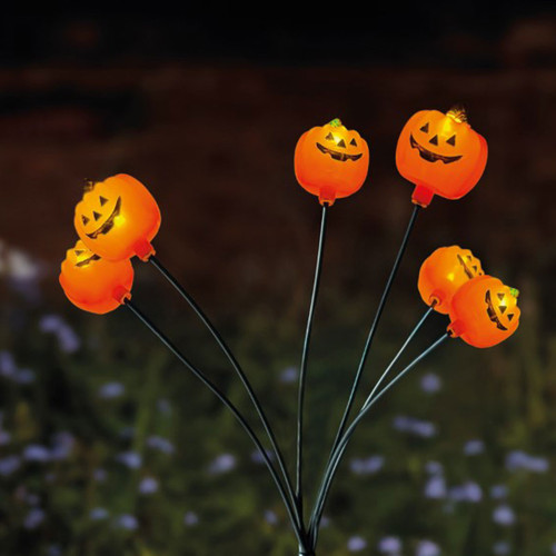 Halloween pumpkin garden stake lights with glowing jack-o'-lantern faces on flexible stems, illuminated outdoors at night for festive seasonal garden decoration.