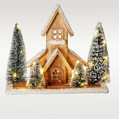 Illuminated wooden Christmas church decoration with warm white LED lights, snow-covered miniature pine trees and frosted detailing, creating a cosy festive tabletop display.