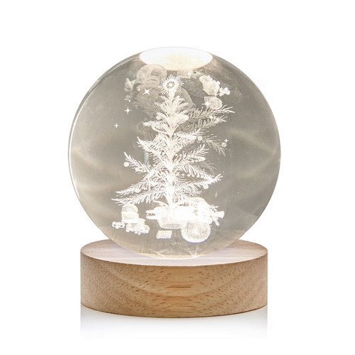 LED crystal ball Christmas decoration featuring an engraved 3D Christmas tree with presents inside a clear glass sphere on a natural wooden base, creating a warm festive ambient light.