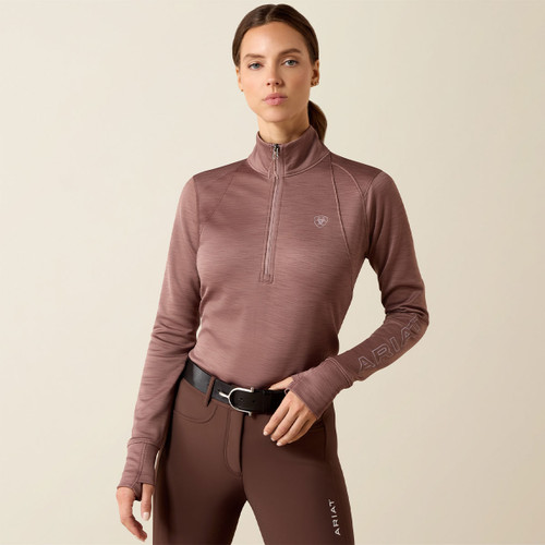 Front view of a model wearing a fitted twilight mauve Ariat half-zip performance pullover with a stand collar, quarter-zip closure, thumbholes, and a tonal chest logo.