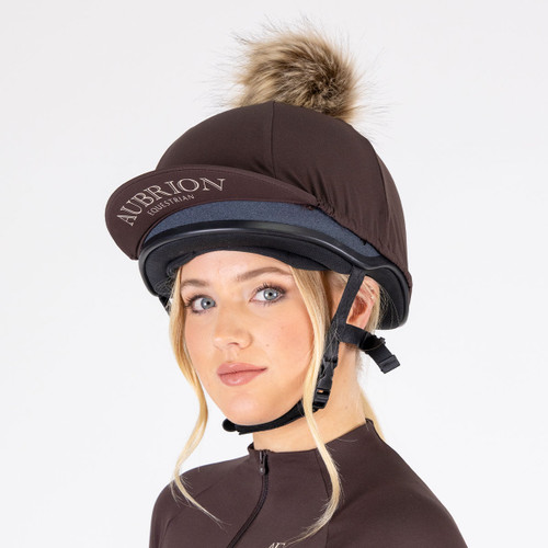 Aubrion espresso riding helmet silk with faux fur pom pom fitted over an equestrian riding helmet.