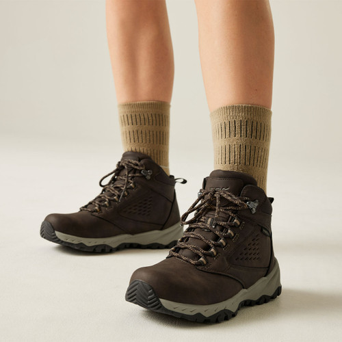 Person wearing brown waterproof hiking boots with cushioned ankle support, rugged grip soles and hiking socks, shown in a front lifestyle view.