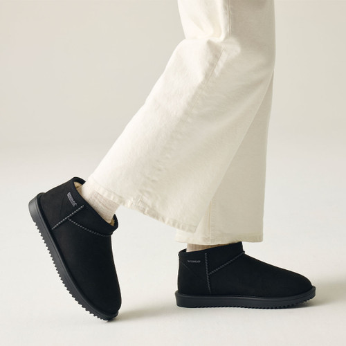 Model wearing black waterproof ankle boots with soft faux fur lining, durable rubber sole and white trousers, shown in a side walking pose.